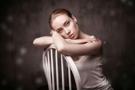 closeup portrait of beautiful woman sitting on a white chair on dakr grey backgroundの写真素材