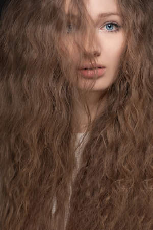 closeup studio portrait of young woman with blue eyes and curly hairの写真素材