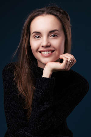 Portrait of young smiling beautiful woman with light makeup over dark blue studio backgroundの写真素材