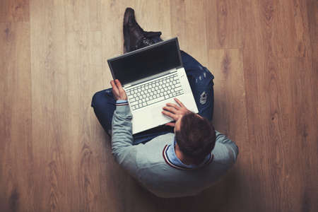 top view of man with laptop sitting on a wooden floor