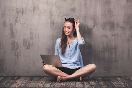 Young smiling woman sitting on the wooden floor with laptopの写真素材