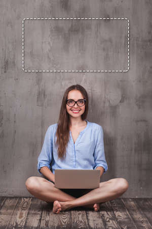Young smiling woman sitting on the wooden floor with laptopの写真素材