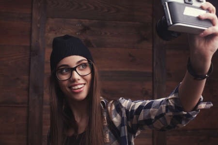 Hipster girl in glasses and black beanie with vintage cameraの写真素材