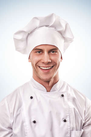 standing smiling male cook in white uniform and hatの写真素材