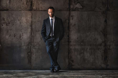 studio portrait of a handsome man wearing black suit on a grunge background.の写真素材