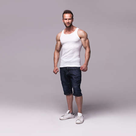 Studio portrait of athletic young man wearing white undershirt isolated on light grey studio backgroundの写真素材