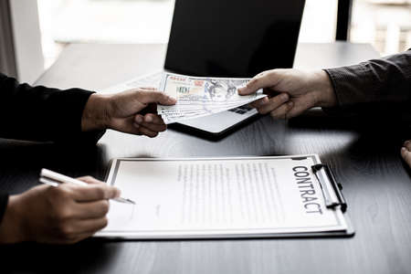 The company's procurement manager is contracting a partner company, accepting large amounts of bribes in dollar bills to cooperate in defrauding the company, fraud is illegal and immoral.の写真素材