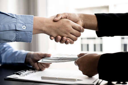 Two businessmen shaking hands and accepting bribes, business partners are working together to corrupt the company by giving them bribes, corruption is illegal and immoral. The concept of corruption.の写真素材