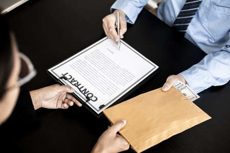 Business men are signing agreements for conspiracy to corrupt and receiving money for bribery in an upcoming big project, corruption is illegal and immoral. The concept of corruption.の写真素材
