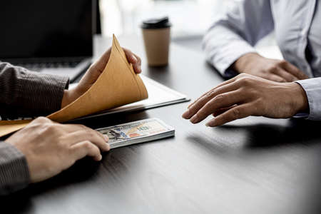 businessman is accepting money from a business partner bringing bribes, a lot of dollars that a partner brings to a businesswoman in her office, bribery is an illegal act. The concept of corruption.の写真素材