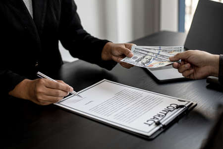 The company's procurement manager is contracting a partner company, accepting large amounts of bribes in dollar bills to cooperate in defrauding the company, fraud is illegal and immoral.の写真素材