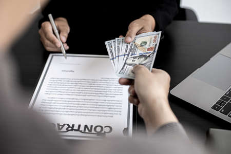 The company's procurement manager is contracting a partner company, accepting large amounts of bribes in dollar bills to cooperate in defrauding the company, fraud is illegal and immoral.の写真素材