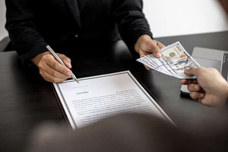 The company's procurement manager is contracting a partner company, accepting large amounts of bribes in dollar bills to cooperate in defrauding the company, fraud is illegal and immoral.の写真素材