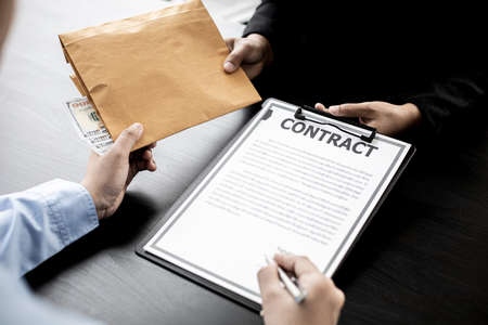 Business men are signing agreements for conspiracy to corrupt and receiving money for bribery in an upcoming big project, corruption is illegal and immoral. The concept of corruption.の写真素材