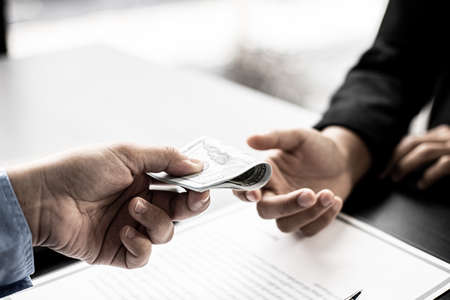 Business men fold the dollar bills and give them to their business partners to bribe an upcoming project, bribery is an illegal and bad practice. The concept of corruption.の写真素材