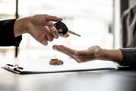 Close up A car rental company employee handing out the car keys to the renter after discussing the rental details and conditions with the renter signing a car rental agreement with the company.の写真素材