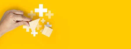 Concept of home insurance. A person's hand is holding a triangular roof, leading to a rectangular wooden block making up the house, with a yellow background. Clipping path and copy space.の写真素材