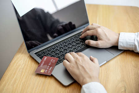 A guy holds a credit card and is filling out his credit card information on his laptop to place an order on the website. Credit cards can be used to pay for goods or services with online merchants.の写真素材