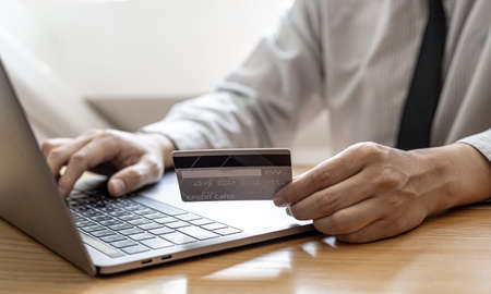 A guy holds a credit card and is filling out his credit card information on his laptop to place an order on the website. Credit cards can be used to pay for goods or services with online merchants.の写真素材