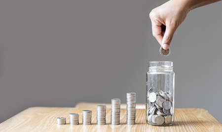 The woman was putting coins into a glass jar with lots of coins and a row of coins on the side. She is saving money every month to invest and spend it in the future. Money saving ideas. copy space.の写真素材