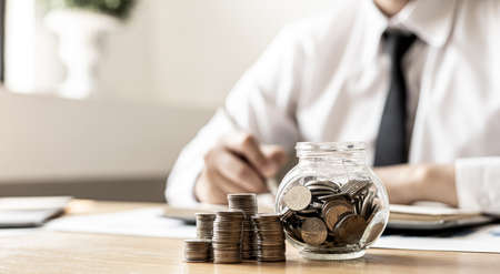 Piles of coins and a glass jar are placed on the desk of a man sitting in keeping a savings account. Placing coins in a row from low to high is a great saving for growth. Money-saving ideas.の写真素材