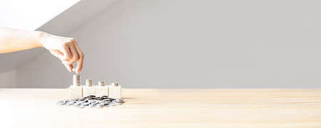 Women are stacking coins on a pile of coins nestled on four rows of square wooden blocks, and many coin piles are placed, individual money-saving ideas. banner background with copy space.の写真素材