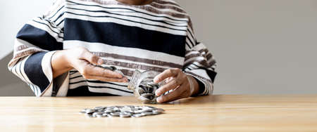 A woman is putting a lot of coins in a glass jar, she is counting the coins she has saved for a long time to put them in the bank. Personal finance concept.の写真素材