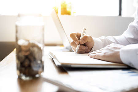A businessman is keeping a record of his income and expenses, he plans his finances by using his monthly savings to buy funds to make it grow faster. Concept of saving money for investment.の写真素材
