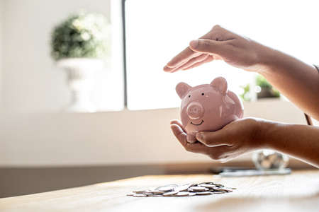 A woman holding a piggy bank in the shape of a pink pig, she is organizing money to divide it into savings and buy funds to make it grow. Personal finance concept.の写真素材