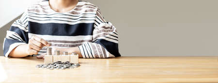 Women are stacking coins on a pile of coins nestled on four rows of square wooden blocks, and many coin piles are placed, individual money-saving ideas. banner background with copy space.の写真素材