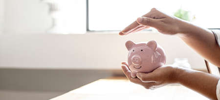 A woman holding a piggy bank in the shape of a pink pig, she is organizing money to divide it into savings and buy funds to make it grow. Personal finance concept.の写真素材