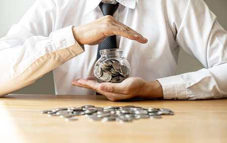 A man holding a jar with a lot of coins inside, he's acting like saving money, saving money will give us money to spend for the future. Personal finance concept.の写真素材