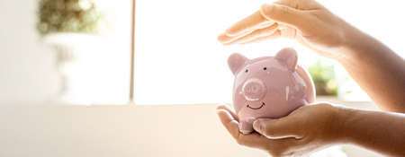 A woman holding a piggy bank in the shape of a pink pig, she is organizing money to divide it into savings and buy funds to make it grow. Personal finance concept.の写真素材