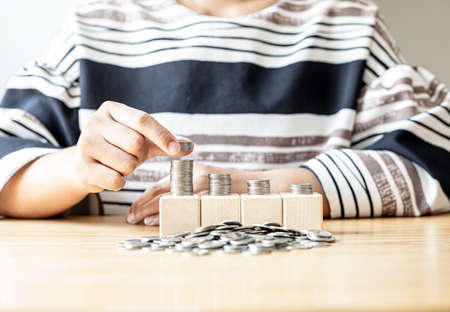 Women are stacking coins on a pile of coins nestled on four rows of square wooden blocks, and many coin piles are placed, individual money-saving ideas.の写真素材