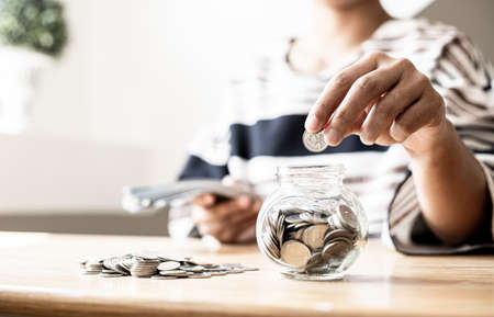 A woman is putting coins in a jar with a lot of coins inside, she is managing to divide her money to save money and invest it to make it grow even more. Concept of saving money and investing.の写真素材