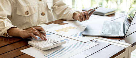 The businesswoman is using a white calculator to check company financial information, she is checking company financial information from the documents provided by the finance department.の写真素材
