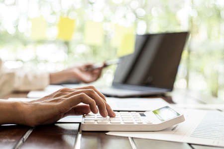Close-up of a businesswoman using a white calculator, a financial businessman examining the numerical data on a company financial document, she uses a calculator to verify the accuracy of numbers.の写真素材