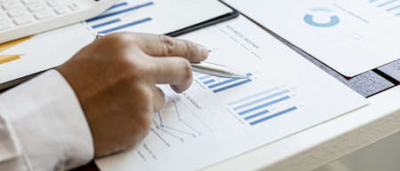 A close-up view of a businessman holding a pen pointing at a bar chart on a corporate finance...