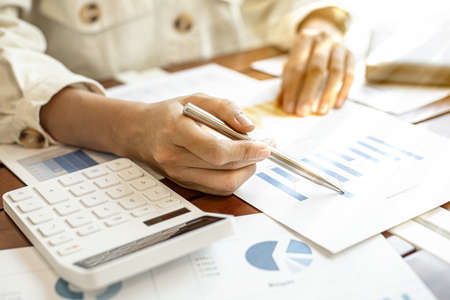 Close-up businesswoman's hand holding a pen pointing at a bar chart on a corporate financial information sheet, the businesswoman examines the financial information provided by the finance department.の写真素材