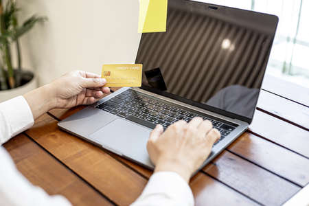 A man holds a credit card and uses a laptop. He is filling out credit card information for online shopping, credit cards can be used to pay for goods and services through physical stores and online.の写真素材