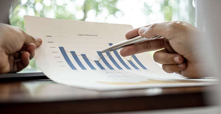 A close-up view of a businessman holding a pen pointing at a bar chart on a corporate finance document, he is meeting with senior management, with the theme of the meeting being Company Finance.の写真素材