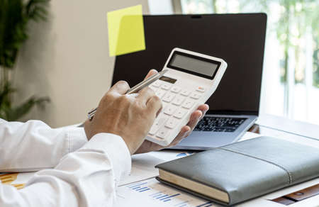 Businessmen press the white calculator to calculate the numbers in the company financial documents, the finance department prepares the document and forwards it to be checked before the meeting.の写真素材