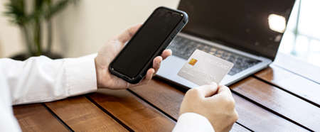 A man holding a smartphone and credit card. He fills his credit card information with a smartphone to pay for the goods ordered on the website, credit cards can pay for goods and services online.の写真素材