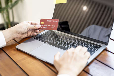 A man holds a credit card and uses a laptop. He is filling out credit card information for online shopping, credit cards can be used to pay for goods and services through physical stores and online.の写真素材
