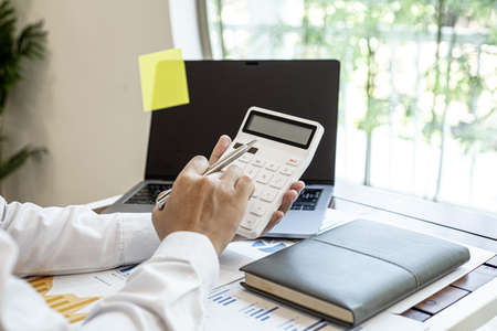 Businessmen press the white calculator to calculate the numbers in the company financial documents, the finance department prepares the document and forwards it to be checked before the meeting.の写真素材