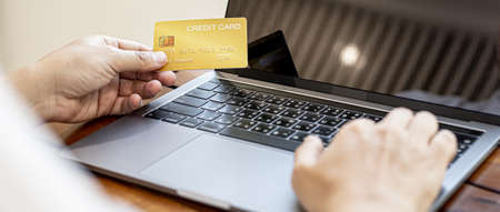 A man holds a credit card and uses a laptop. He is filling out credit card information for online shopping, credit cards can be used to pay for goods and services through physical stores and online.の写真素材