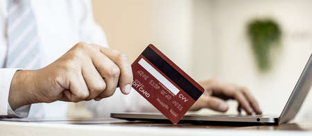 Man is holding a credit card to fill out the information on laptop. They are filling out credit card information for online shopping, credit cards are used to pay for products through online stores.の写真素材