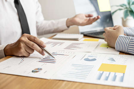 A close-up of a financial businessman holding a pen and pointing at the information sheet on his desk, reading the company's financials to make a financial plan. Financial concept.の写真素材