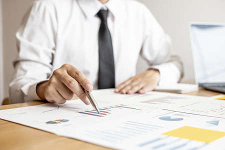 A close-up of a financial businessman holding a pen and pointing at the information sheet on his desk, reading the company's financials to make a financial plan. Financial concept.の写真素材
