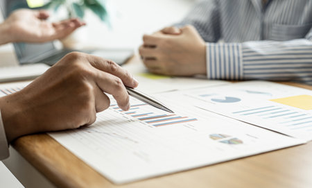 A close-up of a financial businessman holding a pen and pointing at the information sheet on his desk, reading the company's financials to make a financial plan. Financial concept.の写真素材